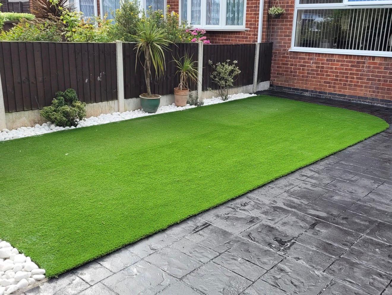 Artificial grass with stamped concrete patio and white pebble border in rear garden