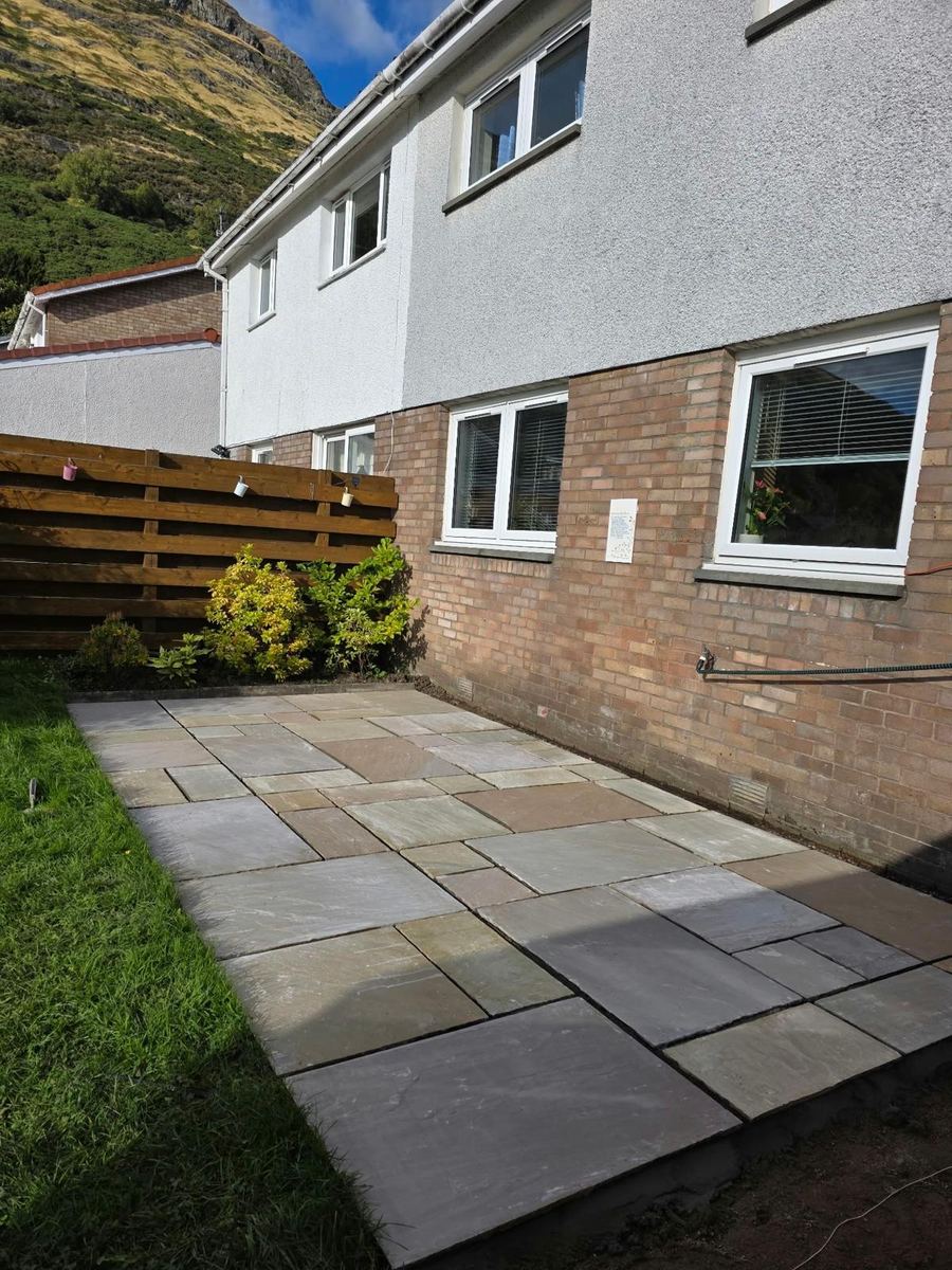 New Indian sandstone patio running along the side of a house next to the lawn